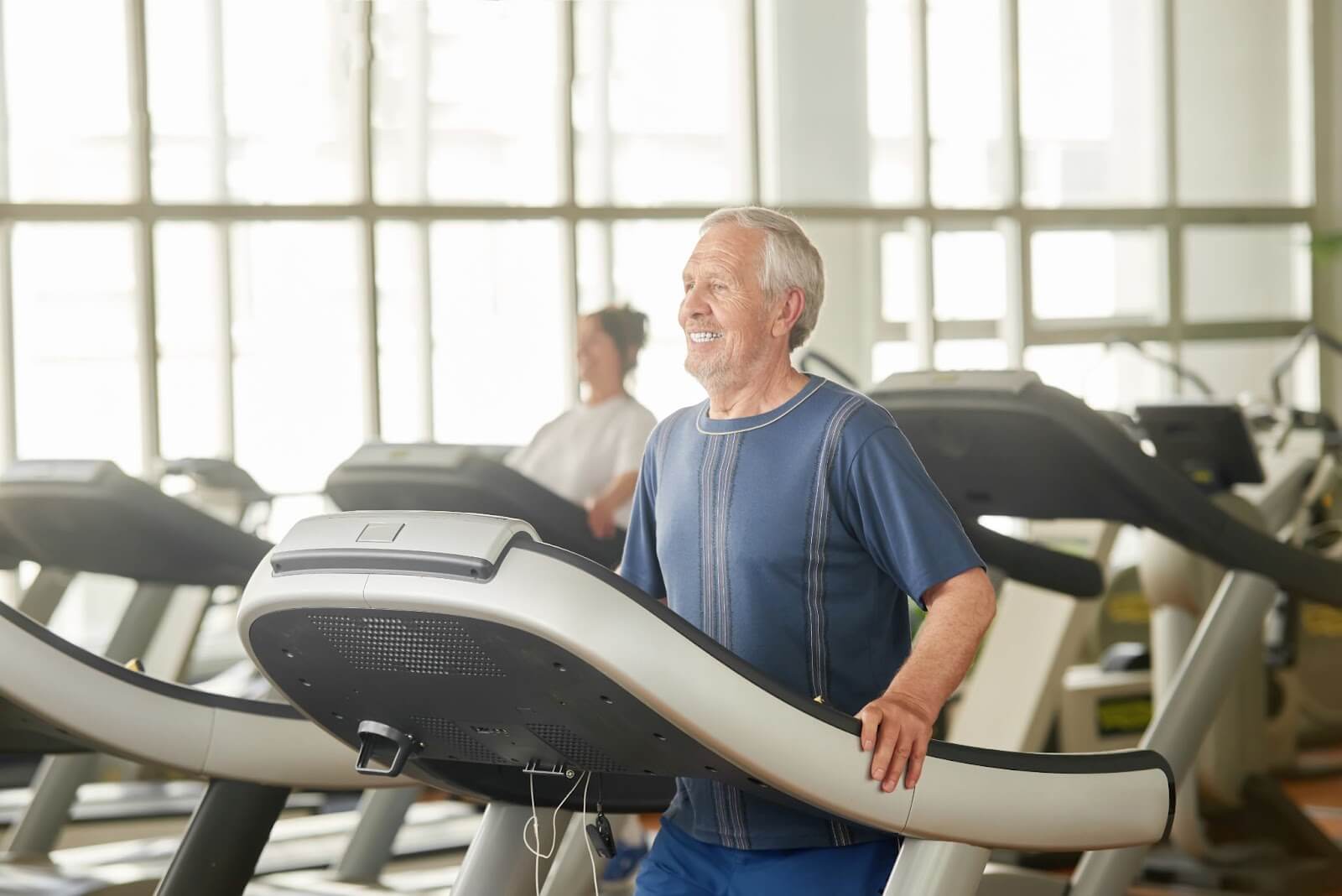 Aging adult smiling in the gym while exercising on a treadmill